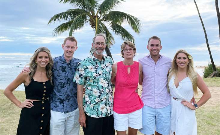 A family of six people – three women, three men – posing for the camera on a tropical beach.